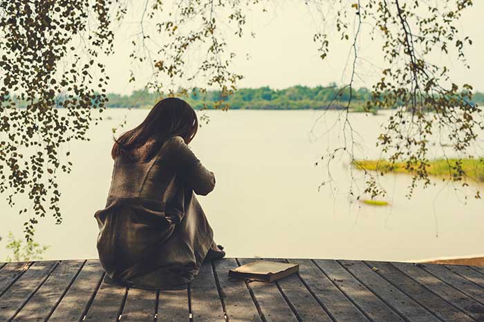 אישה יושבת לבד על שפת הנהר